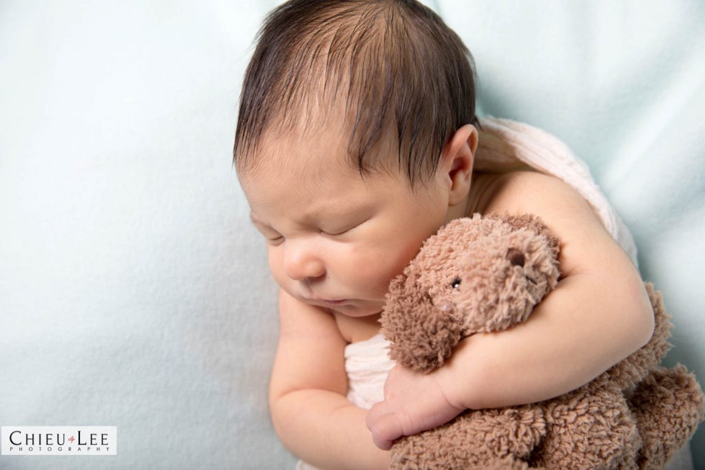 Closeup newborn baby boy sleeping eyes closed white wrap cuddling holding hugging plush puppy doll toy on white blanket