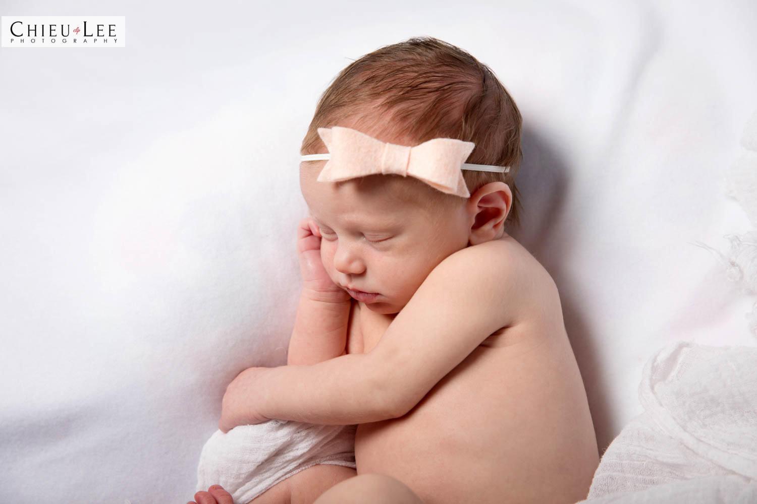 Newborn baby girl sleeping eyes closed pink bow headband half body on white blanket
